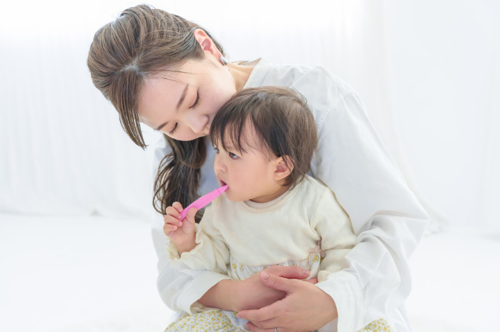 歯ブラシを自分で持って加える赤ちゃんと見守る母親