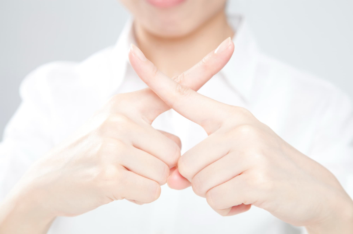 指でバツを作る女性の手元