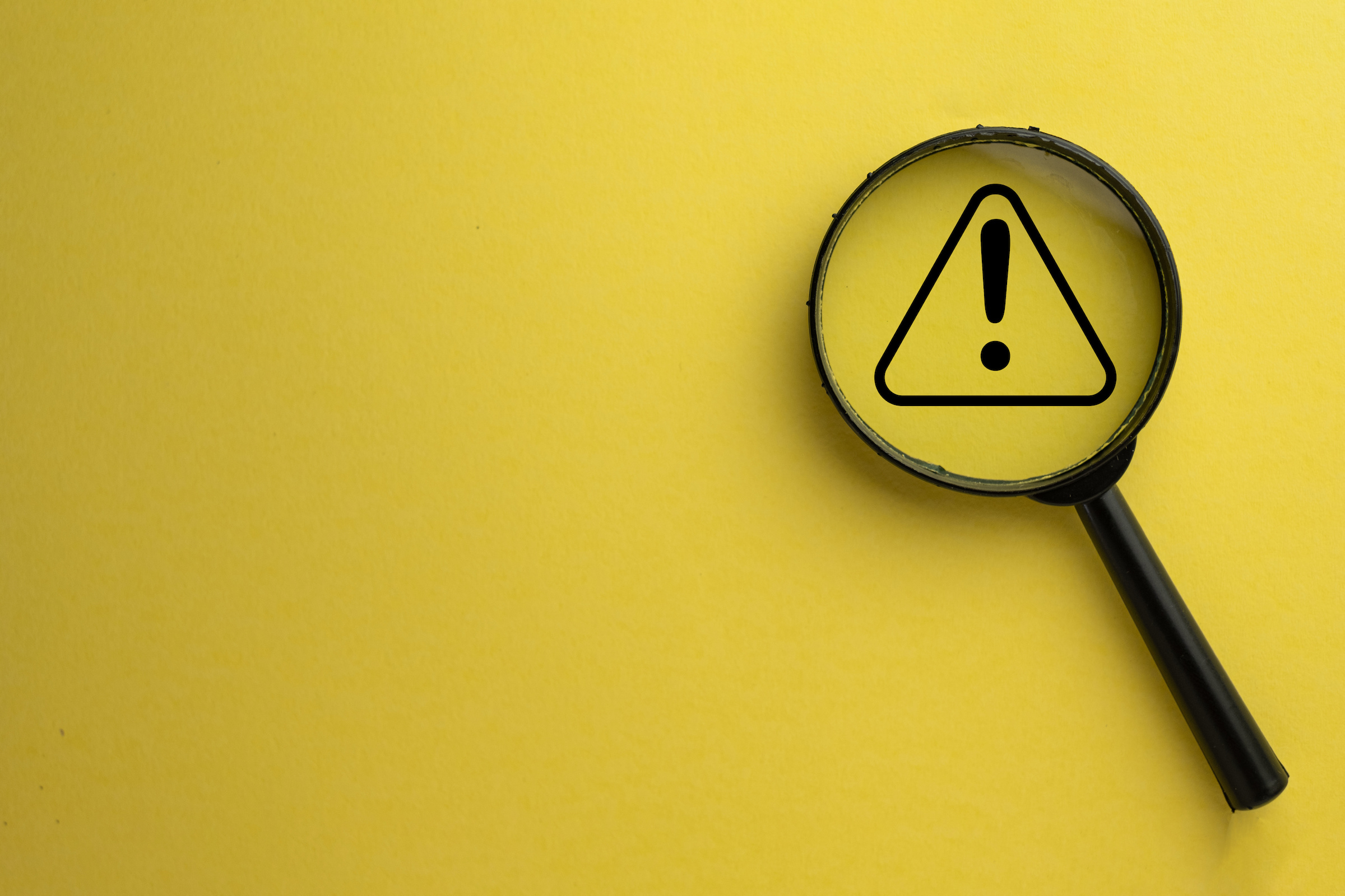 Attention sign,Exclamation mark,warning sign concept.,Magnifying glass focus on Hazard warning attention sign icon over yellow background with copyspace.